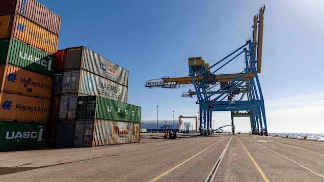 Stacks of shipping containers and a large crane on a shipping pier. 