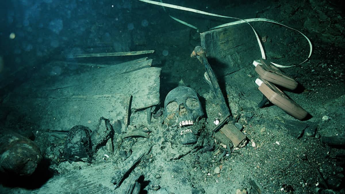 Merenpojassa lojuvia laivanhylyn esineitä ja niiden keskellä ihmisen luita, muun muassa pääkallo. 