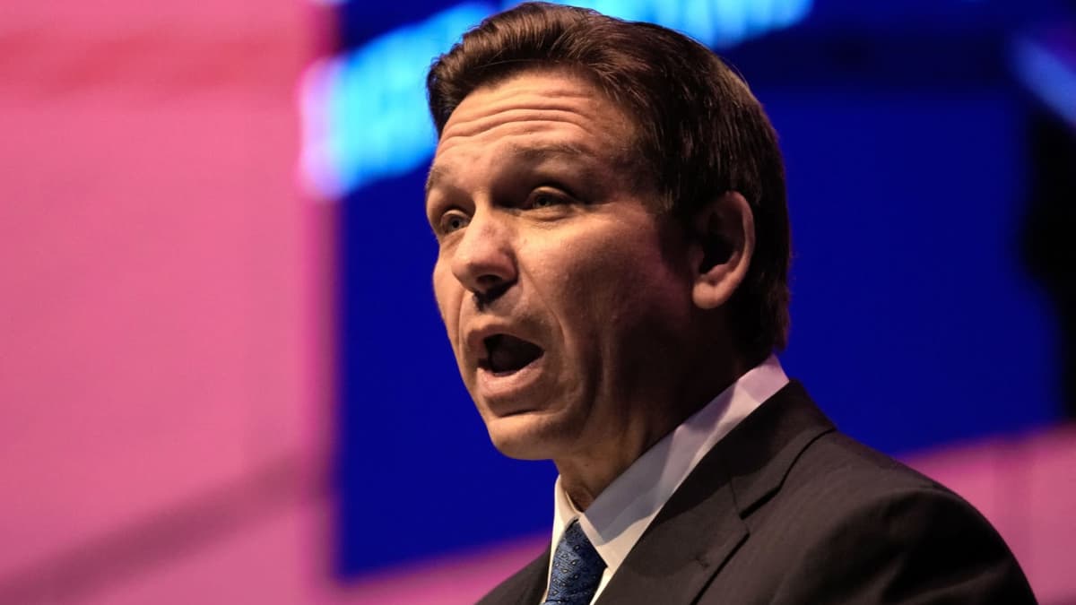 Floridan kuvernööri Ron DeSantis puhuu konferenssissa, tausta sininen ja vaalenapunainen.