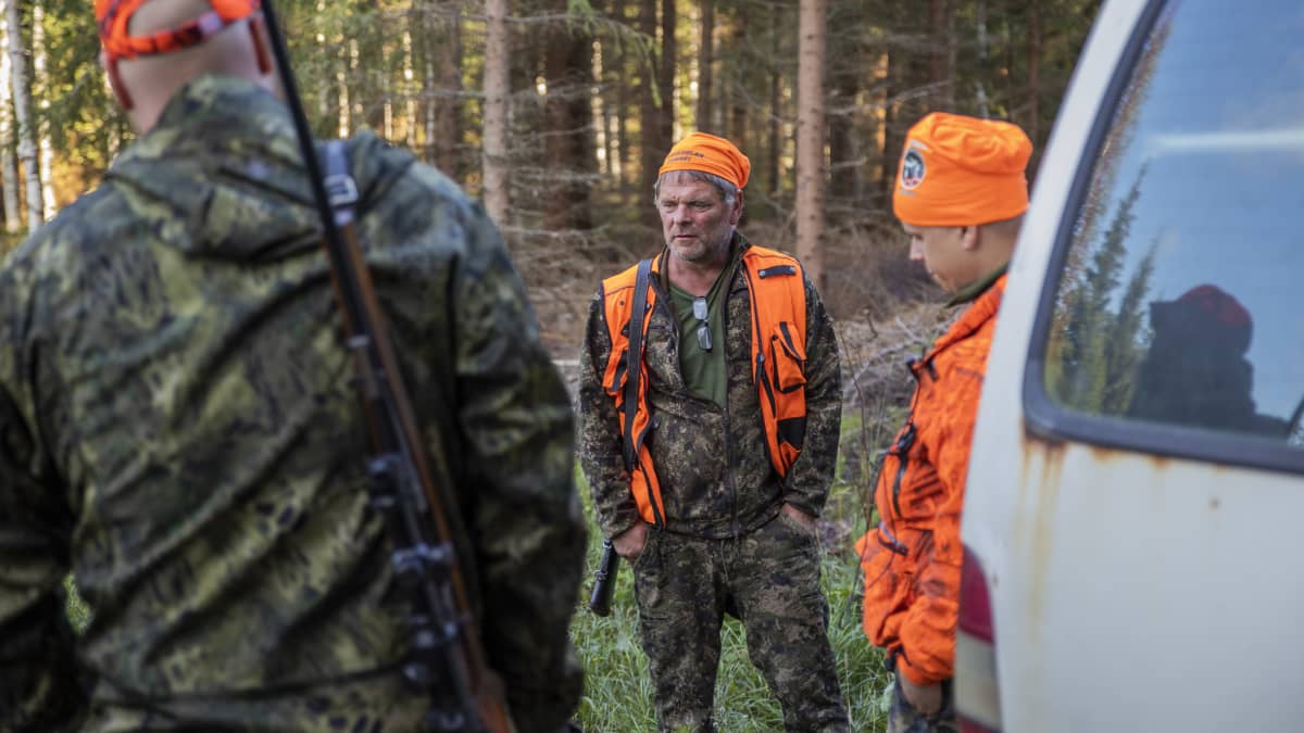 Metsästäjät Ilpo Suoknuuti, Miro Oikarinen ja Aapo Takala juttelevat ringissä metsässä.