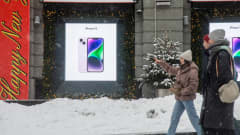 Ihmisiä kavelee lumisella kadulla. Taustalla iphone-puhelimen mainos.