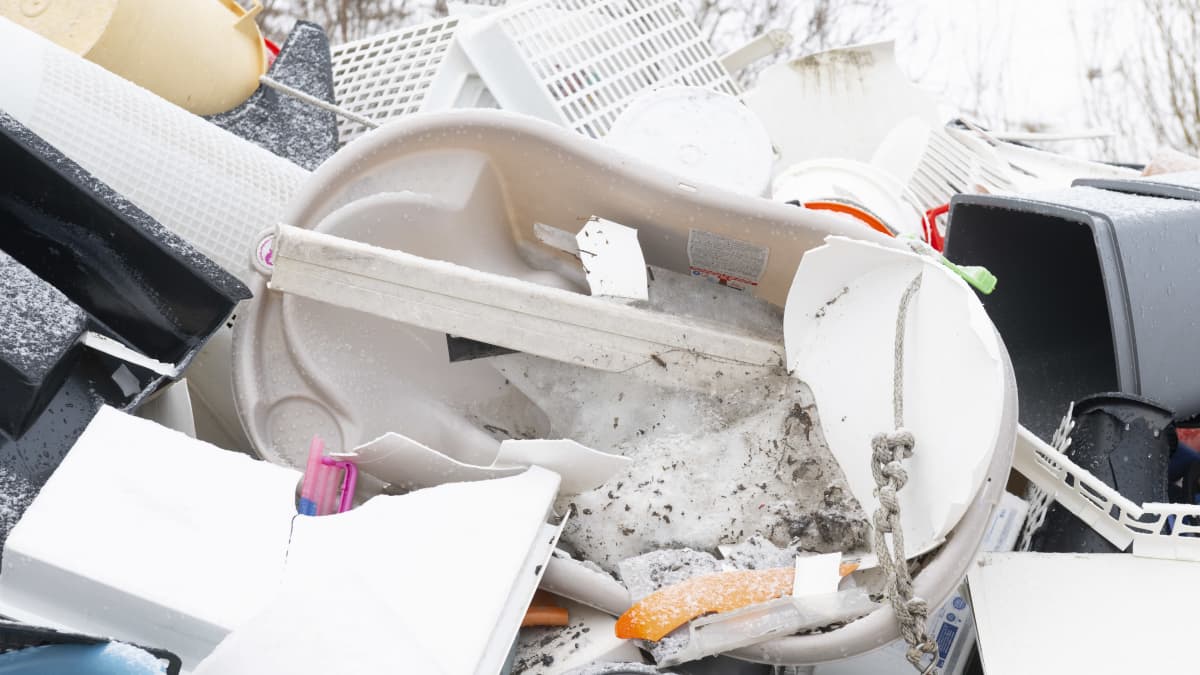 Rikkinäinen, muovinen lasten kylpyamme kaatopaikalla muovitavaran seassa. 