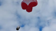Kuvassa Ilmatieteen laitoksen punainen ja heliumtäytteinen mittauspallo taivaalla. Pallossa roikkuu vaijereiden päässä mittauslaitteita. 