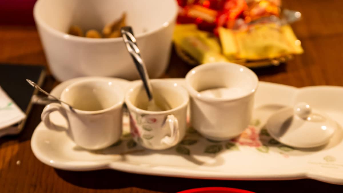 Pöydällä näkyy pieniä espresso-kahvikuppeja sekä lautasella naposteltavaa, ilmeisesti manteleita tai joitakin pähkinöitä.