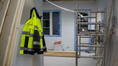 Keltainen työtakki roikkuu naulassa. Taloa rakennetaan. 