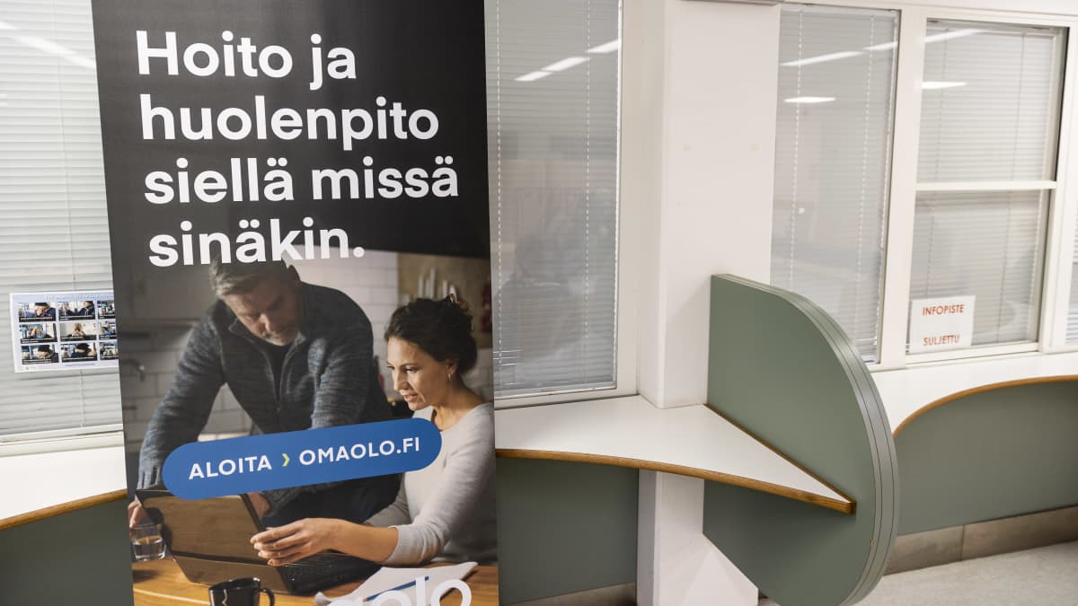 Terveyskeskuksen toimiston edessä juliste, jossa lukee "Hoito ja huolenpito siellä missä sinäkin. Aloita - omaolo-fi". Viereisessä pisteessä lappu "Infopiste suljettu".