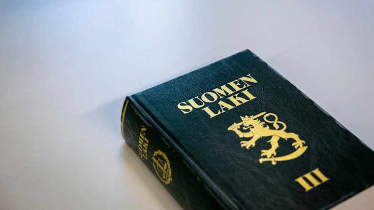 A thick, hardbound book of Finnish law with a gilt lion and the words "SUOMEN LAKI III" on the cover.