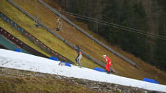 Kaksi hiihtäjää hiihtää ladulla. Ladun ympäristö on täysin paljas lumesta.