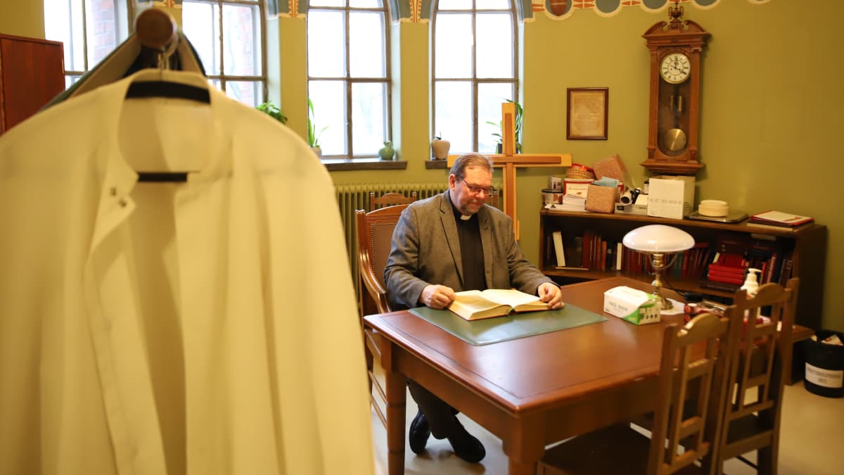 Pappi lukee raamattua pöydän ääressä
