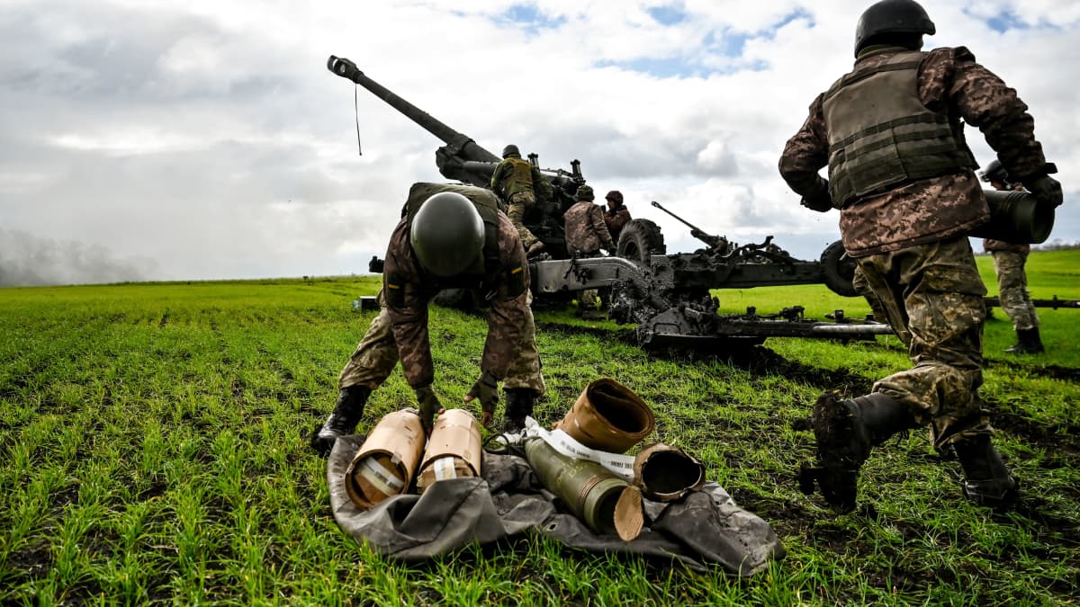 Ukrainalaissotilaat lataavat tykkiä, etualalla ammuksia, vihreä pelto. 
