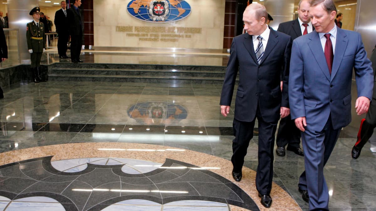 Putin ja Ivanov kävelevät GRU:n rakennuksen aulassa ja katsovat lattiaa, johon on maalattu GRU:n symboli, lepakon kuva.