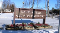 En skylt med texten Närpes stad står i en blomrabatt. Marken är täckt av snö.