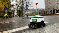 A green-and-white delivery robot crossing a damp city street in the autumn.
