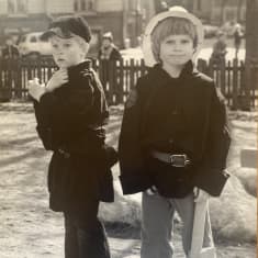 Nokikolariksi ja palomieheksi pukeutuneet Aapo Rista ja Tuomas Heikkilä seisovat leikkipuiston pöydällä, taustalla aita ja sen takana isompia lapsia.