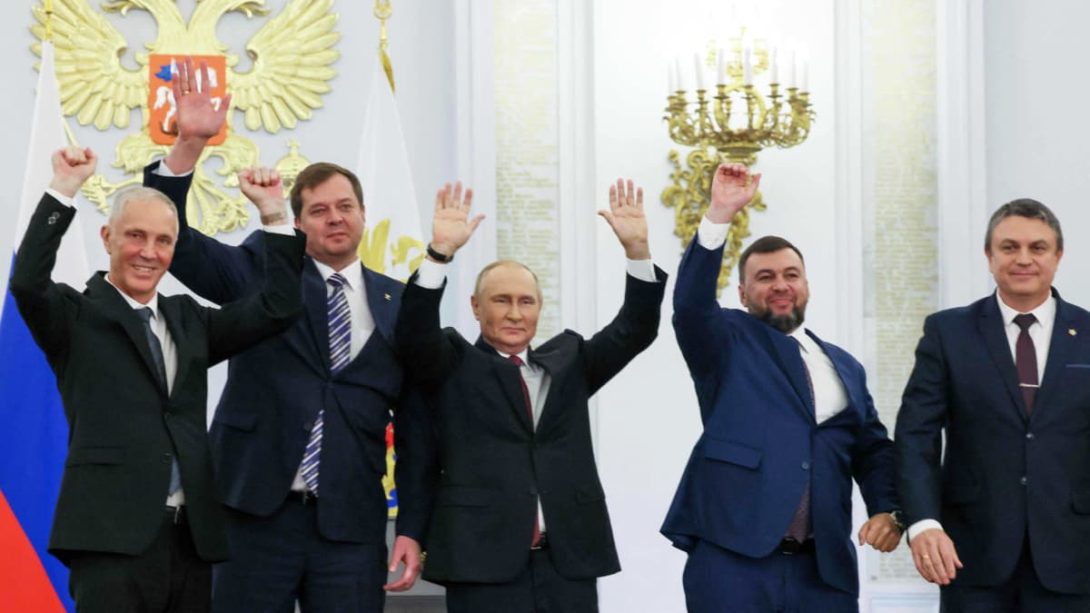 Viisi miestä seisoo rivissä kädet ylhäällä.