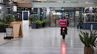 Food courier riding a bike down an empty shopping centre hallway.