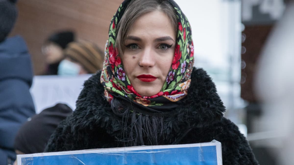 Nainen pitää sinikeltaista kylttiä, jossa lukee että hän on venäläinen, mutta tukee (ukrainalaisia).