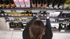 Myyjä asettelee viinipulloja Alkon hyllylle Kuopion Savilahden Alkossa. 