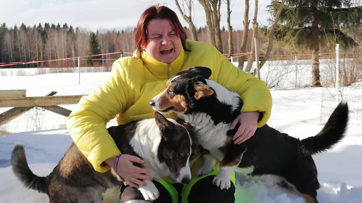 Jenni Ekoluoma istuu lumihangella kaksi koiraa sylissään.