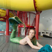 Merenneidon pyrstöön pukeutunut mies makoilee uimahallin lattialla.