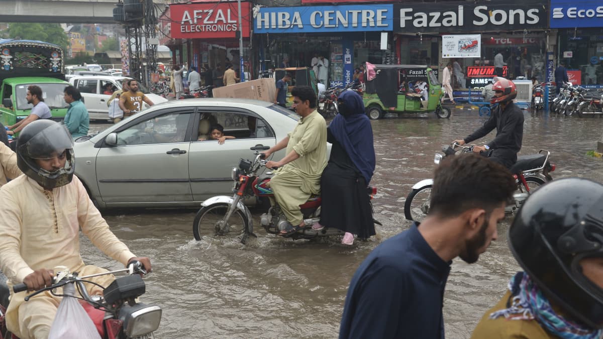 Ihmiset ajavat autoilla ja mopoilla tulvivalla tiellä.