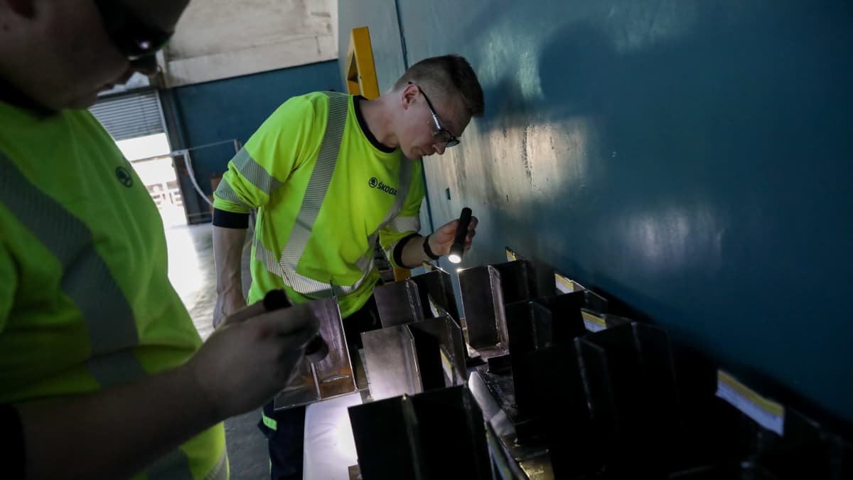 Kaksi keltaliivistä miestä tutkii metallikyhäelmiä taskulampulla. 
