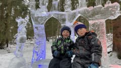Lapset Olli ja Miska Hakala istuvat jäätaideteoksen jäisen penkin päällä.  