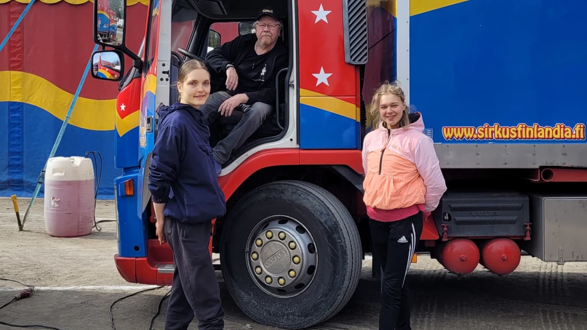 Kaksi naista seisoo Sirkus Finlandian rekan edustalla, mies istuu rekan nupissa.