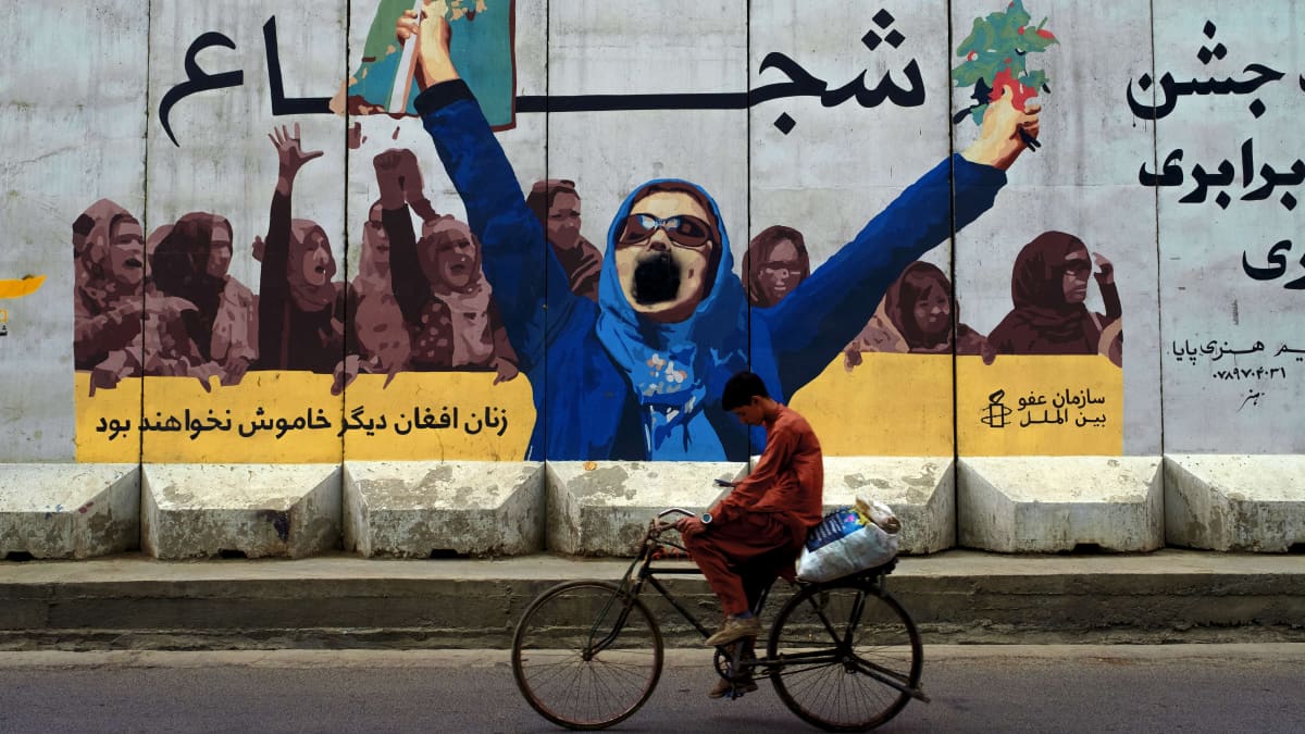 Ihminen pyöräilee seinämaalauksen ohi, jossa nainen huutaa kädet ilmassa etualalla ja taka-alalla joukko naisia pitää banderollia jossa on tekstiä ja Amnesty internationalin logo.