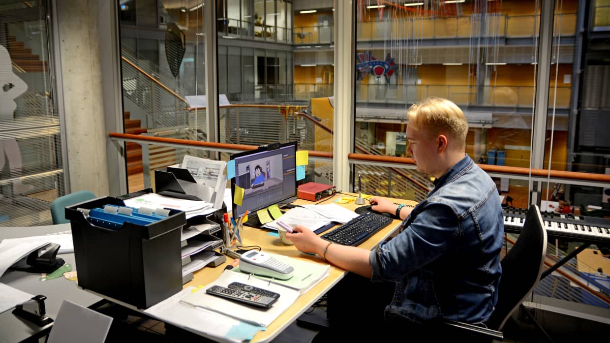 Animaation tekijä Tuomas Toivainen istuu tietokoneen äärellä, taustalla yliopiston lasinen sisäseinä.