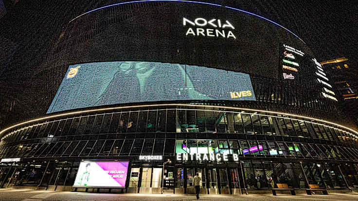 A nighttime view of a large curving black building with signs saying Nokia Area, Entrance B and Ilves. 