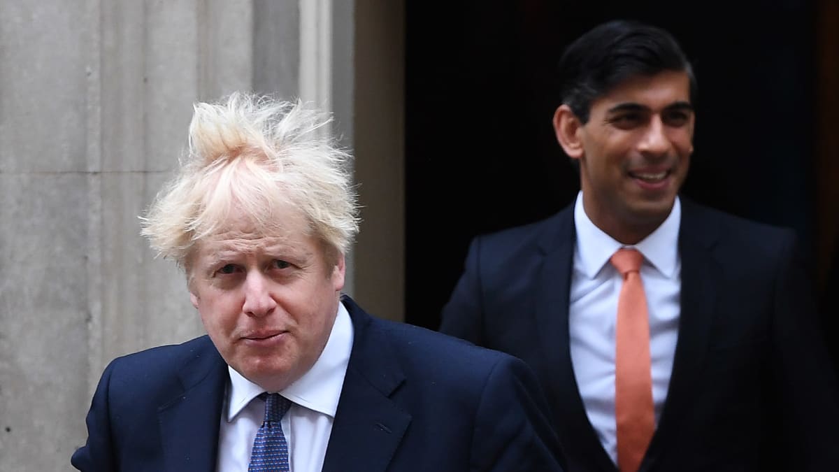 Boris Johnson tukka pystyssä. Taustalla Rishi Sunak.