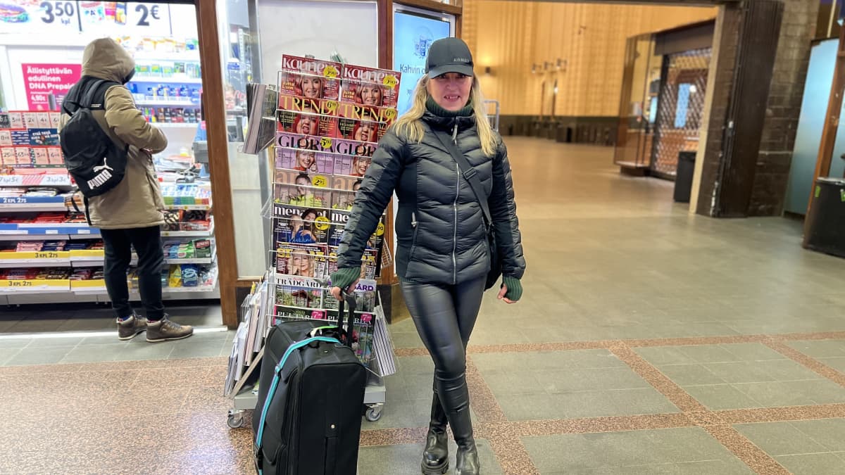 Nainen seisoo matkalaukkunsa kanssa Helsingin päärautatieasemalla.