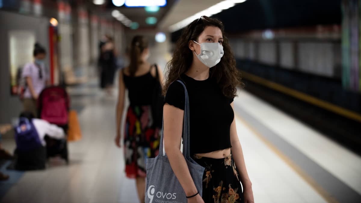 Nainen odottaa metroa maski päässään.
