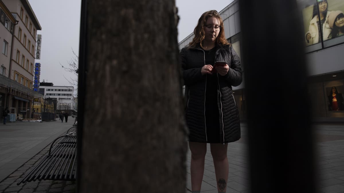 Juulia Savolainen katsoo puhelintaan ja seisoo Kuopion torin lähellä olevalla kävelykadulla.