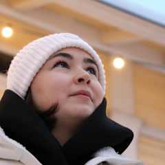 Tummahiuksinen nainen valkoisissa talvivaatteissa katsoo yläviistoon.