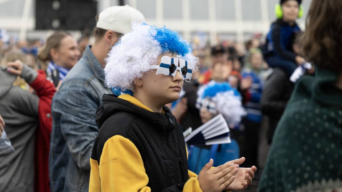 Nuori kisafani taputtamassa. Päässään pojalla on Suomen lipun värinen peruukki ja aurinkolasit.