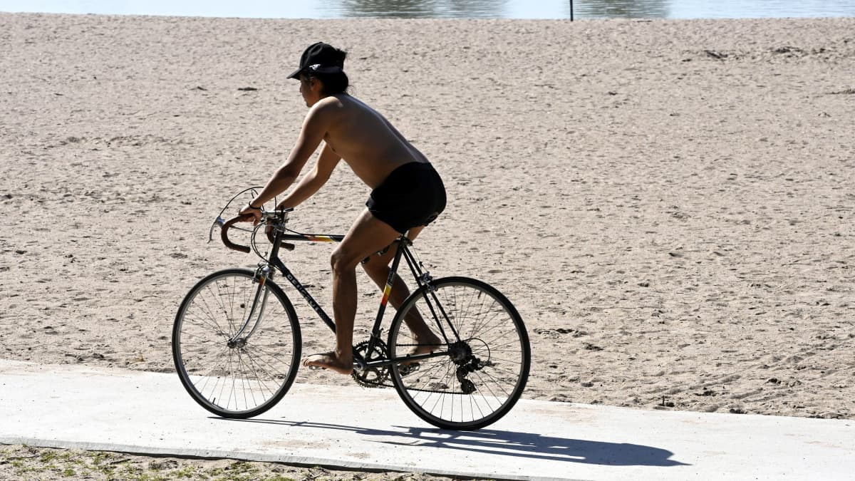 Paidaton mies ajaa polkupyörällä uimarannalla.