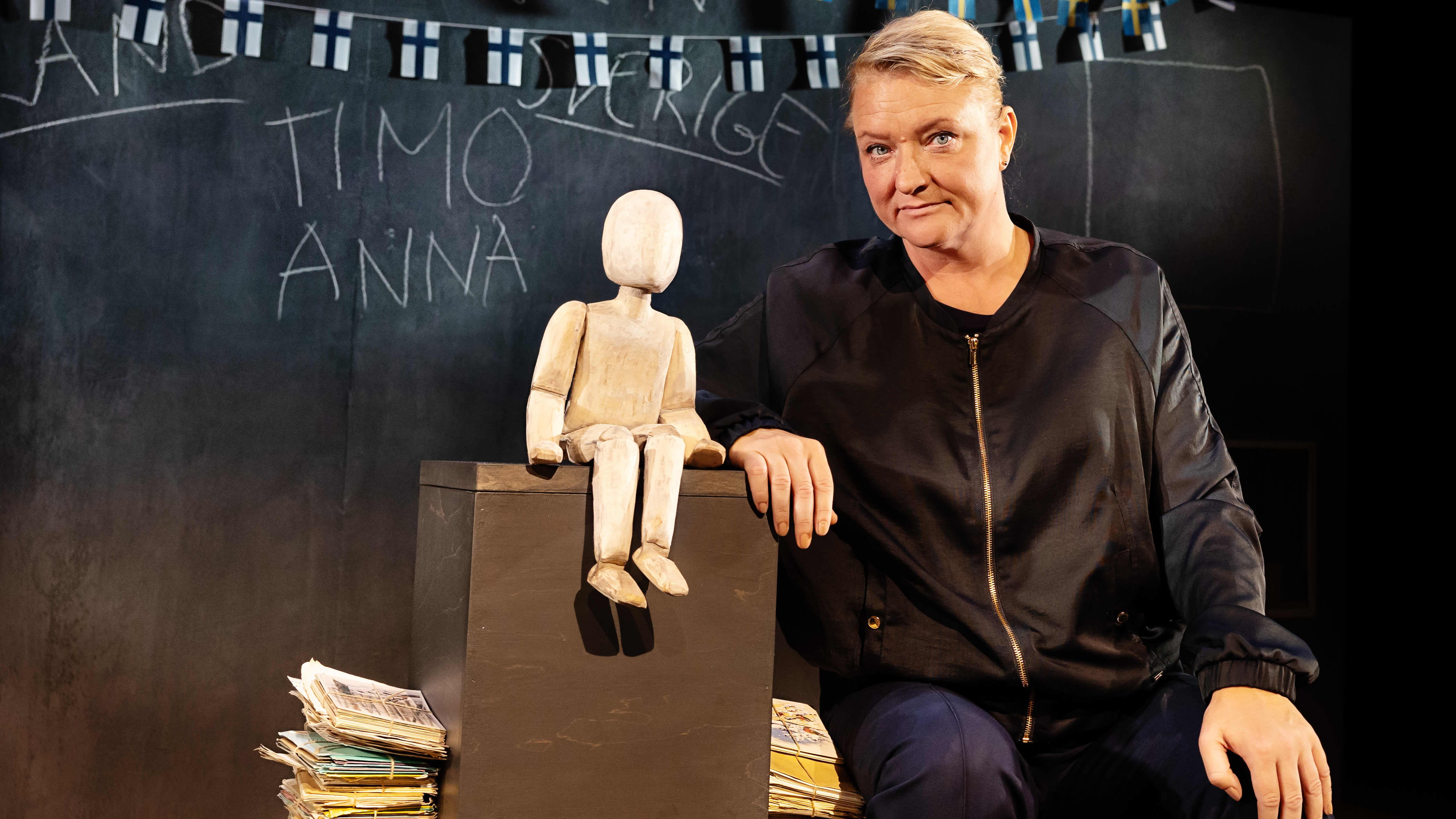 Anna Takanen istuu Lilla Teaternin näyttämöllä harjoitustauolla. Takanaan liitutaulu, jossa roikkuu Suomen ja Ruotsin lippuja. Hän esittää monologia, joka pohjautuu omiin kokemuksiin sotalapsen lapsena.