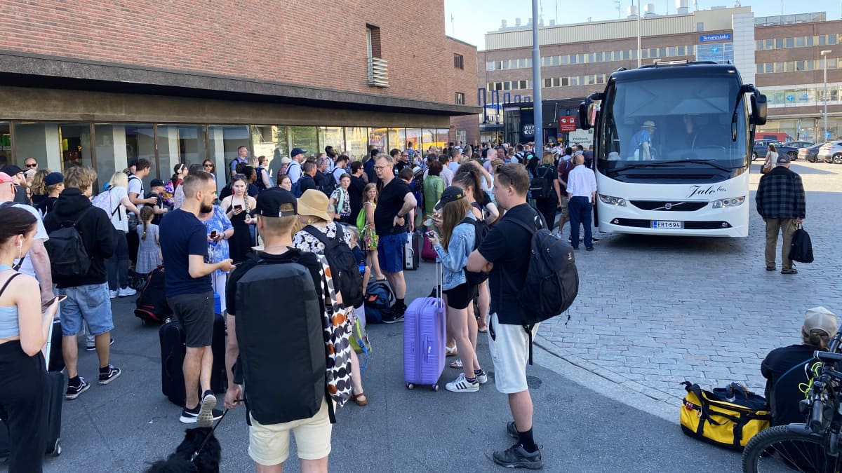 Ihmisiä seisoo joukkona Tampereen rautatieaseman edessä. Yksi bussi ottaa matkustajia sisään.