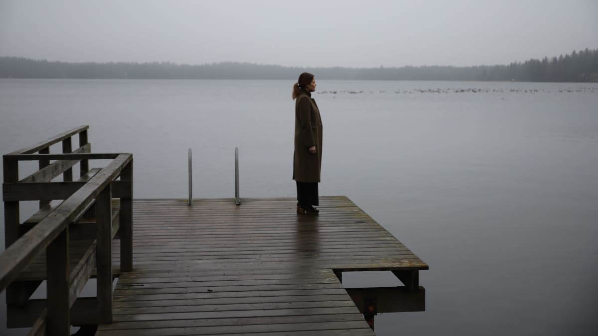 nainen seisoo laiturilla, katselee sumuiselle järvelle
