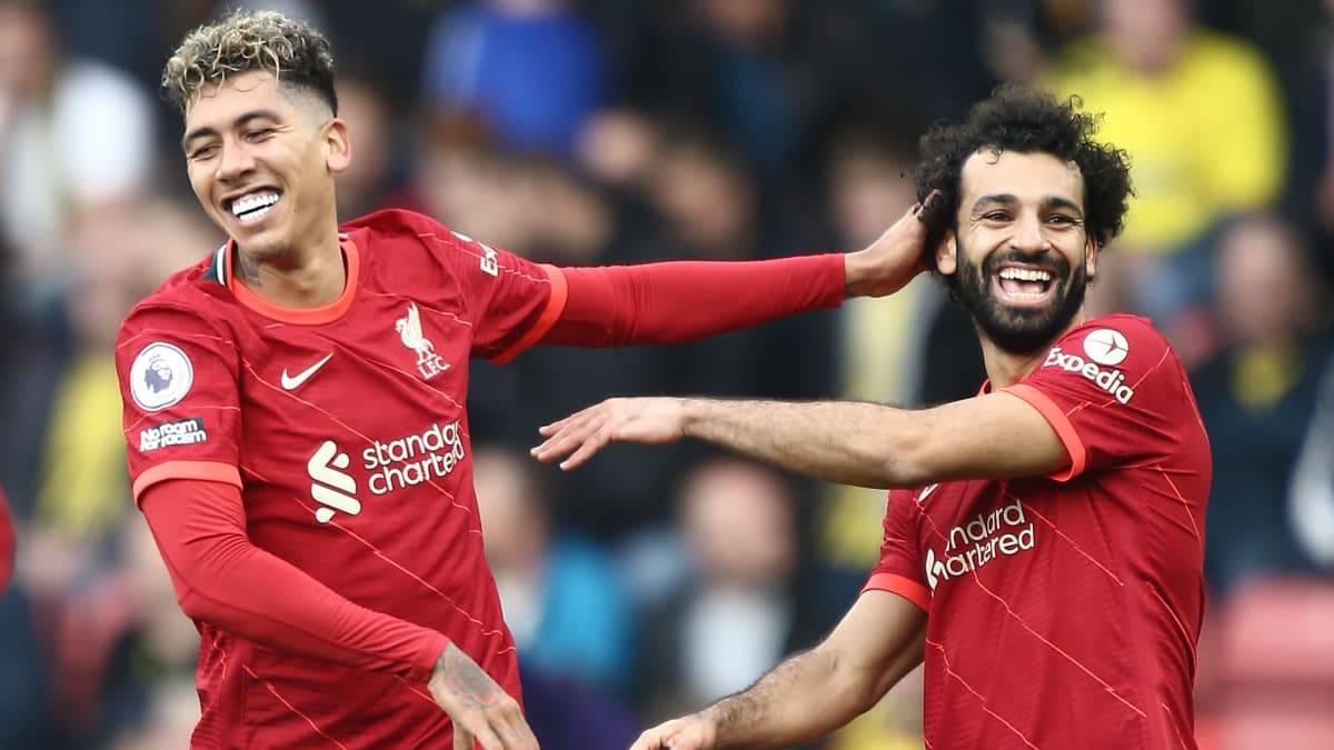 Roberto Firmino ja Mohamed Salah hymyilevät iloisesti ja tuulettavat maalia punaisessa Liverpoolin peliasussa.
