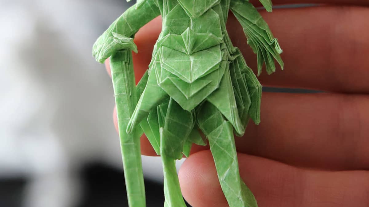 Vihreä ihmishahmoinen origamiveistos Juho Könkkölän kädessä.