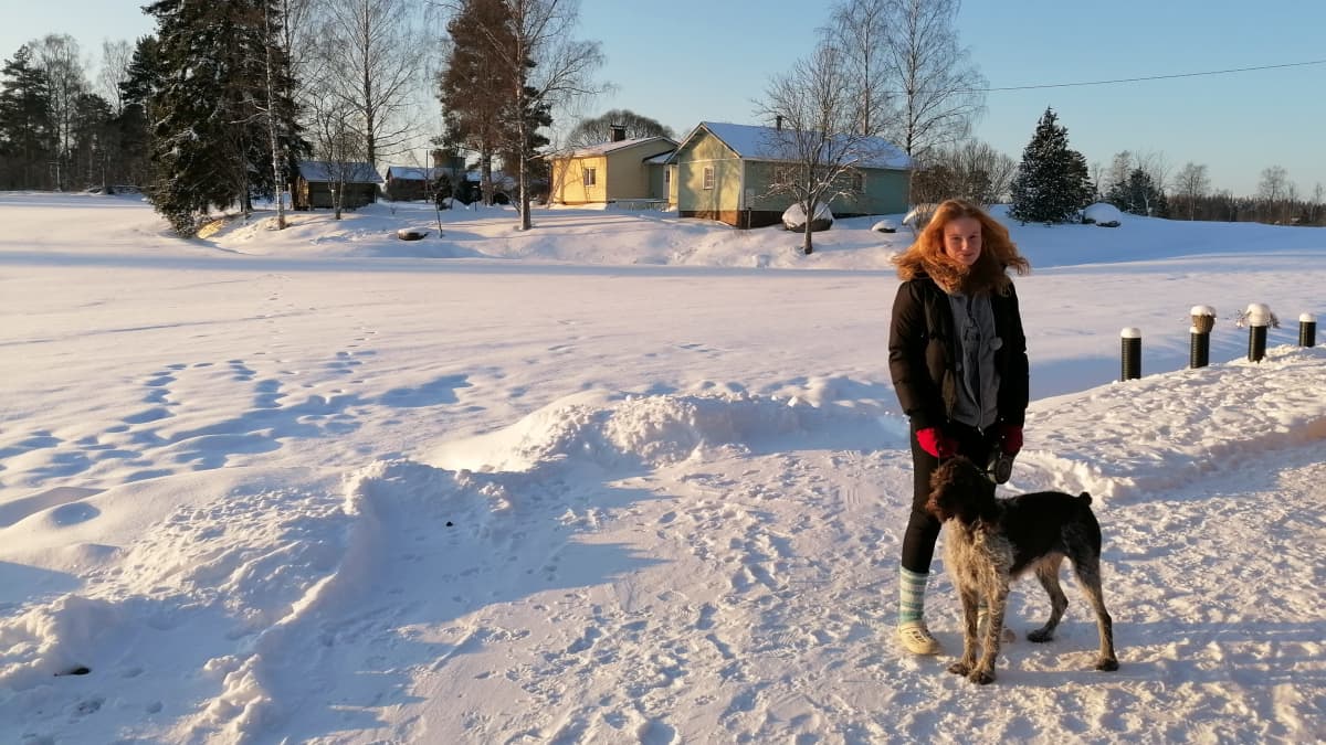 Tyttö ja iso koira seisovat lumisen pellon laidalla