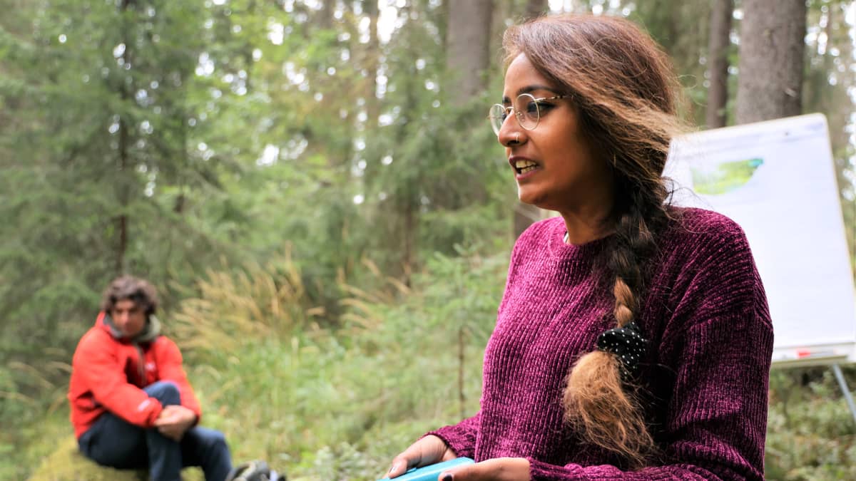 Go green routes-verkoston koordinaattori Shreya Utkarsh seisoo fläppitaulun edessä metsässä.