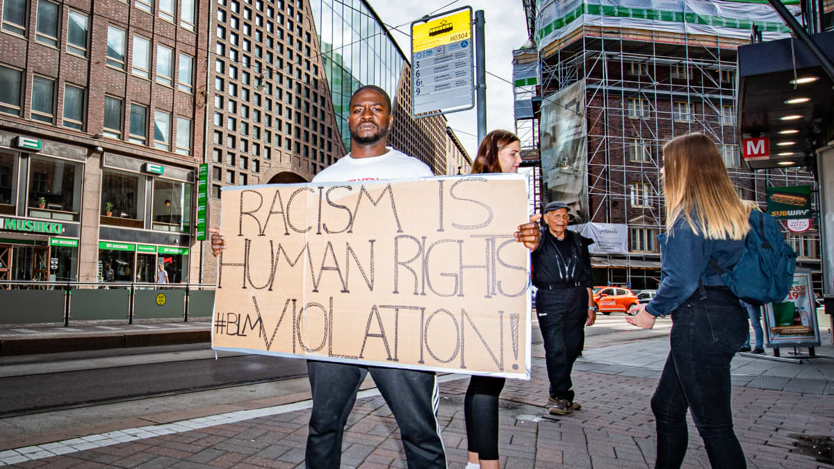Arnold Siku pitelee kylttiä jossa lukee "Racism is human rights violation".