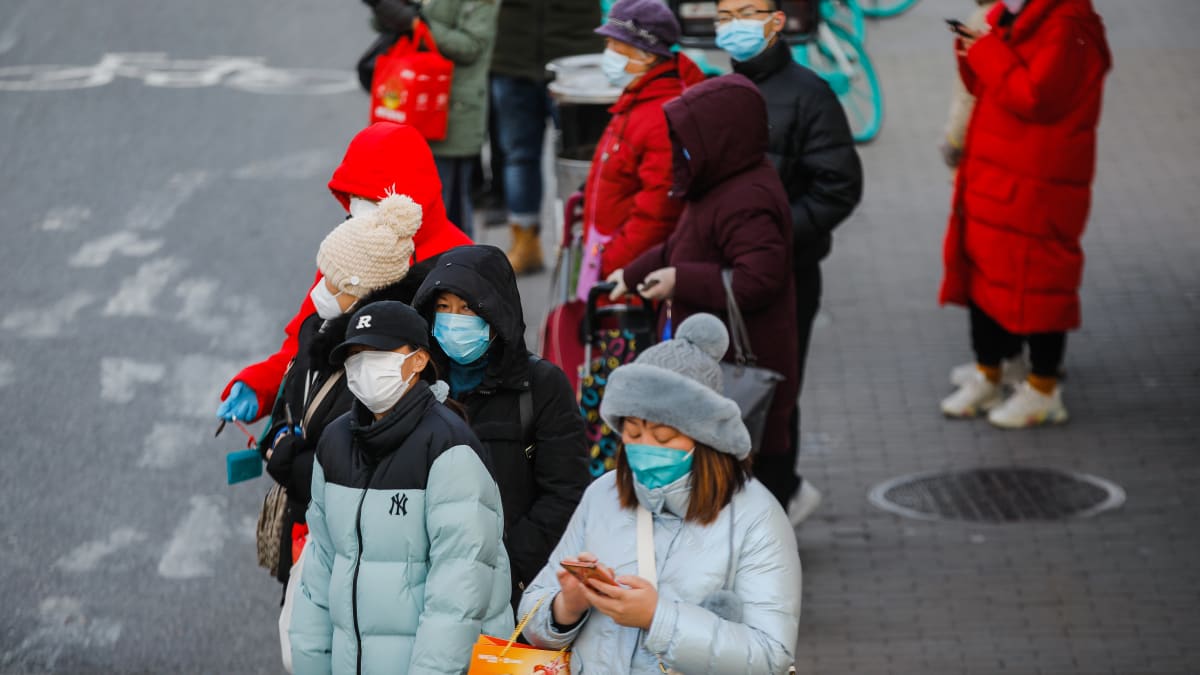 Ihmisiä kasvomaskeineen odottamassa bussia linja-autoasemalla Pekingissä, Kiinassa, 14. joulukuuta 2022.