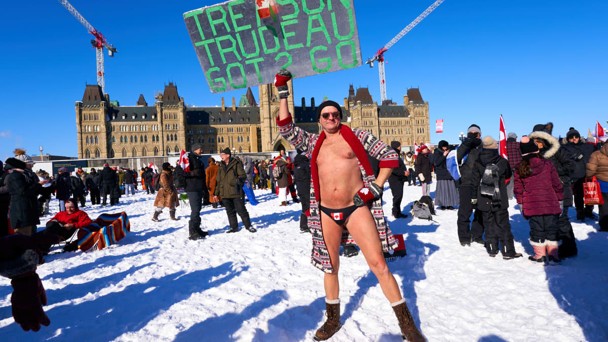 En demonstrant i badbyxor står i snön framför Kanadas parlament. Han bär ett plakat som anklagar Kanadas premiärminister för landsförräderi.