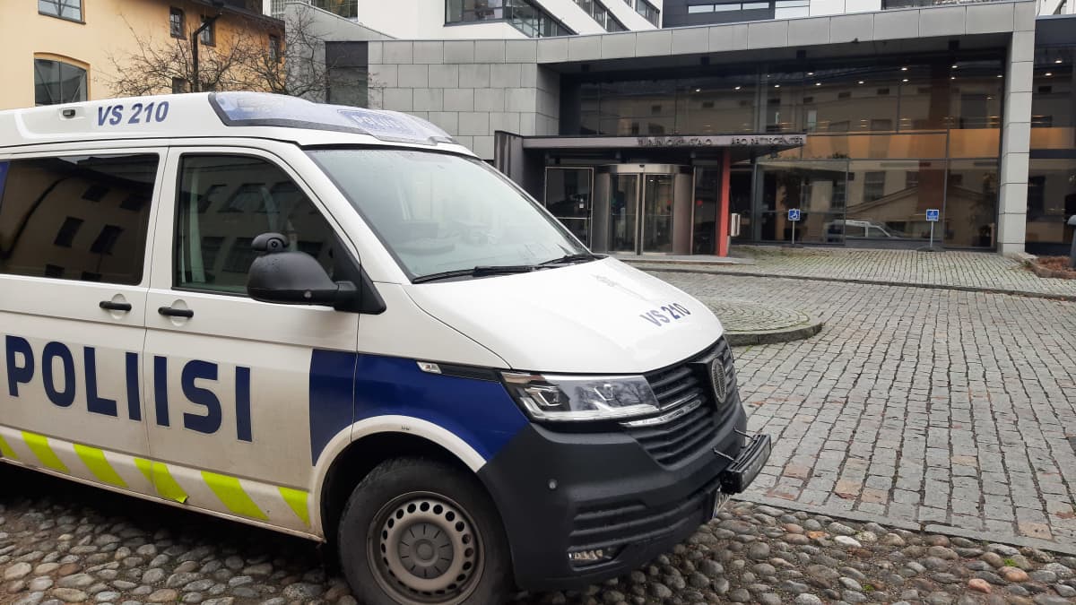 En polisbil står parkerad på en stenlagd innergård vid ett hus med glasväggar. Ovanför ingången finns texten Turun oikeustalo Åbo rättscenter.