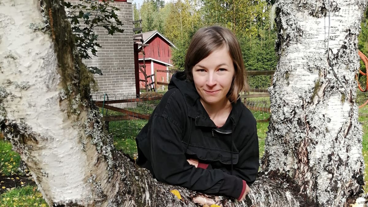Hanna-Kaisa Härme nojaa pihapuuta vasten syksyisessä maisemassa.